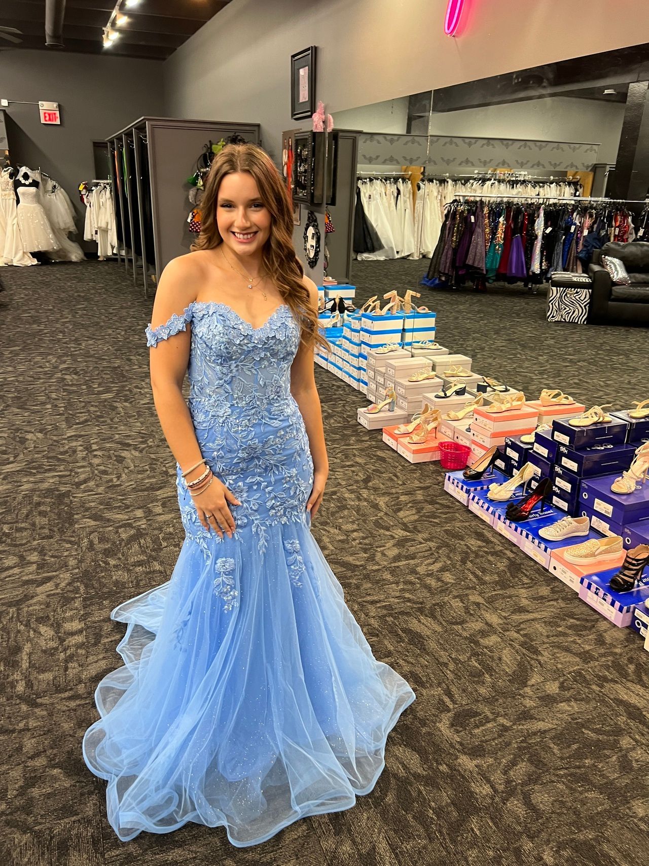 Woman in a light blue off-the-shoulder gown stands in a dress shop.