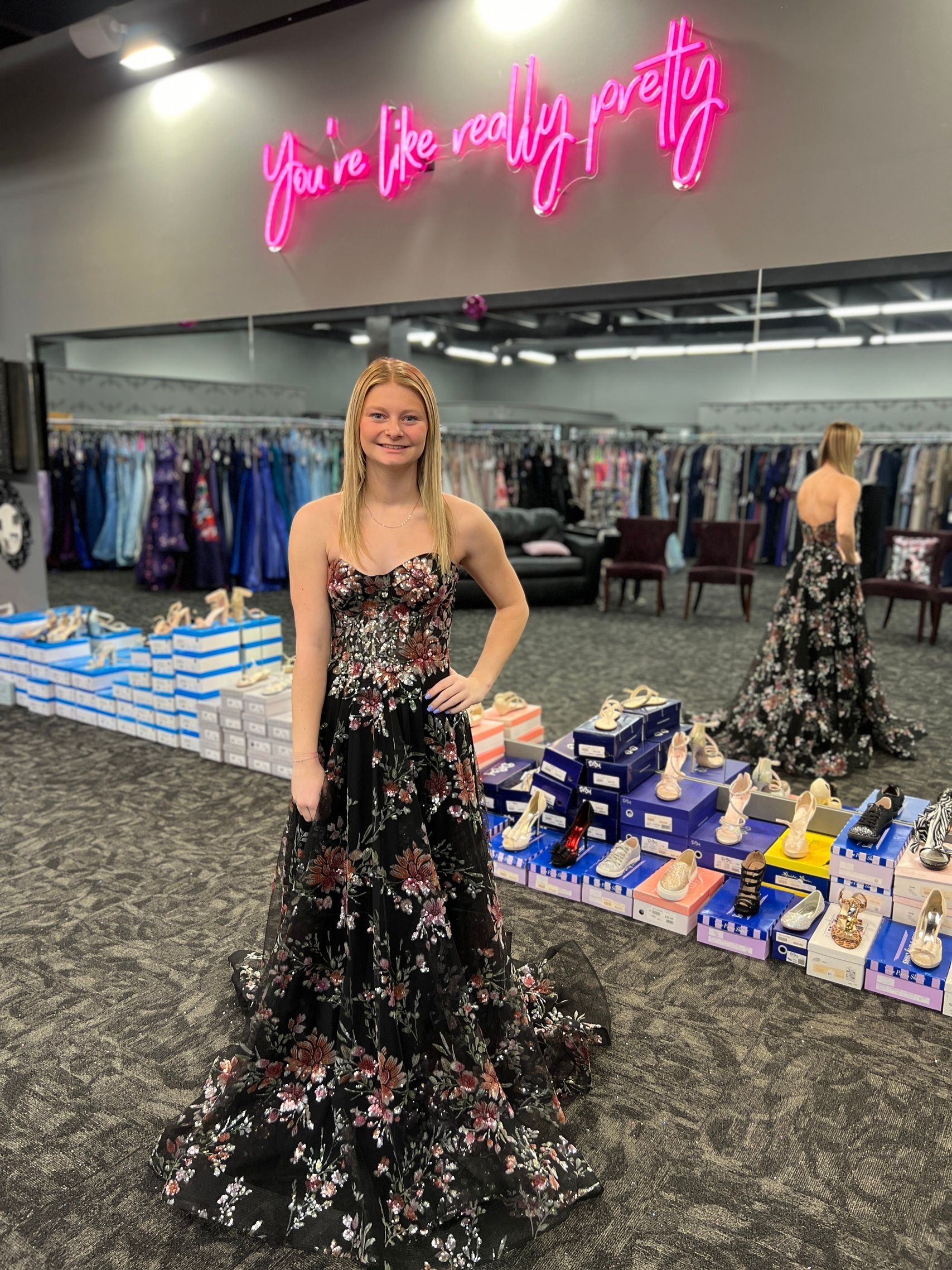 Woman in floral gown in a dress shop; neon sign