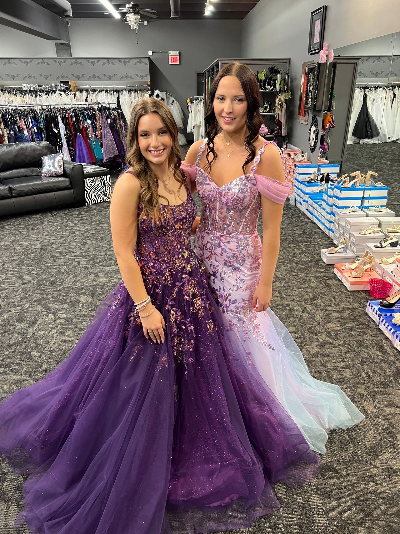 Two women in formal gowns posing in a dress shop.