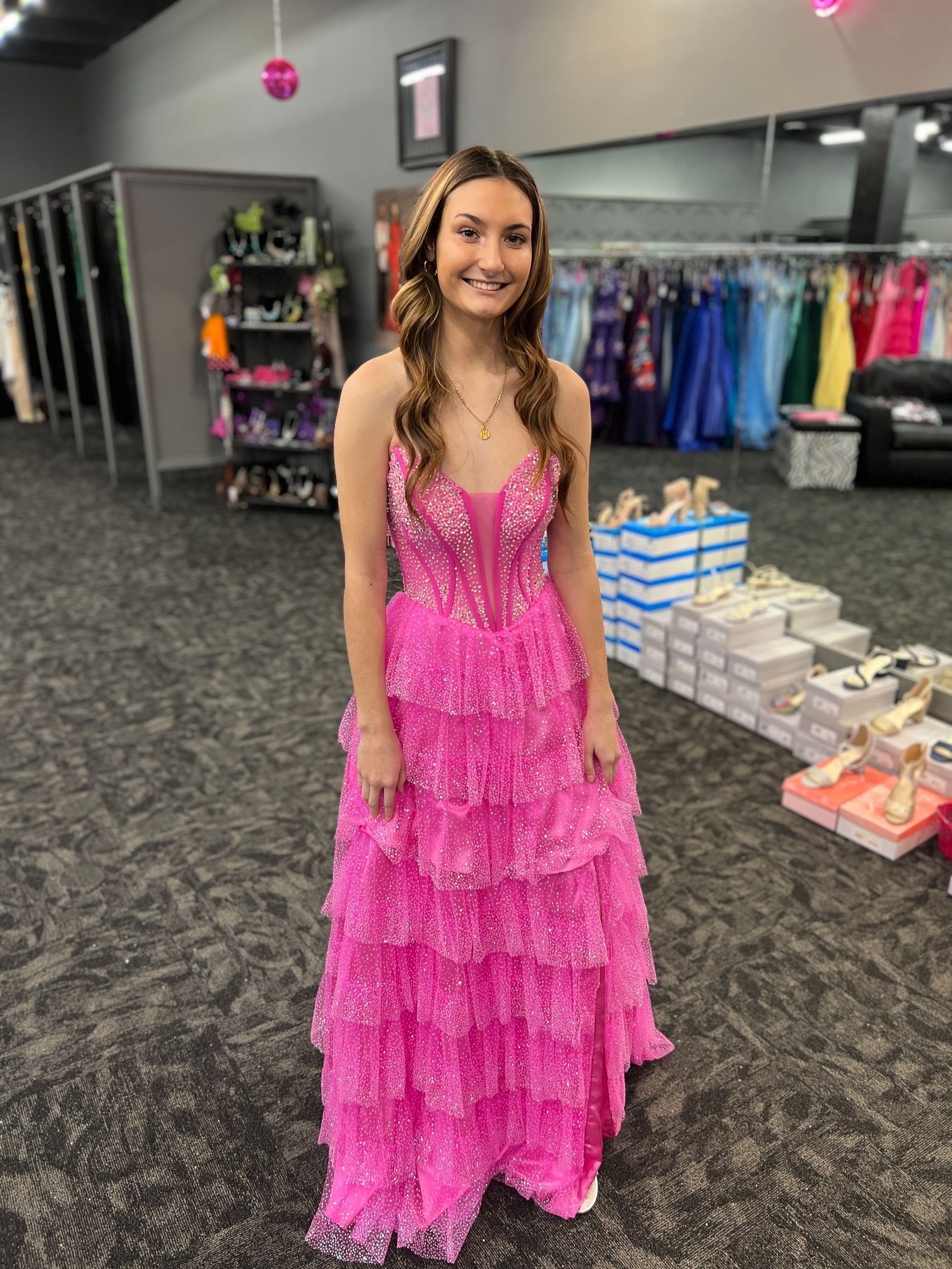 Woman in a pink, tiered, formal dress in a dress shop, smiling.