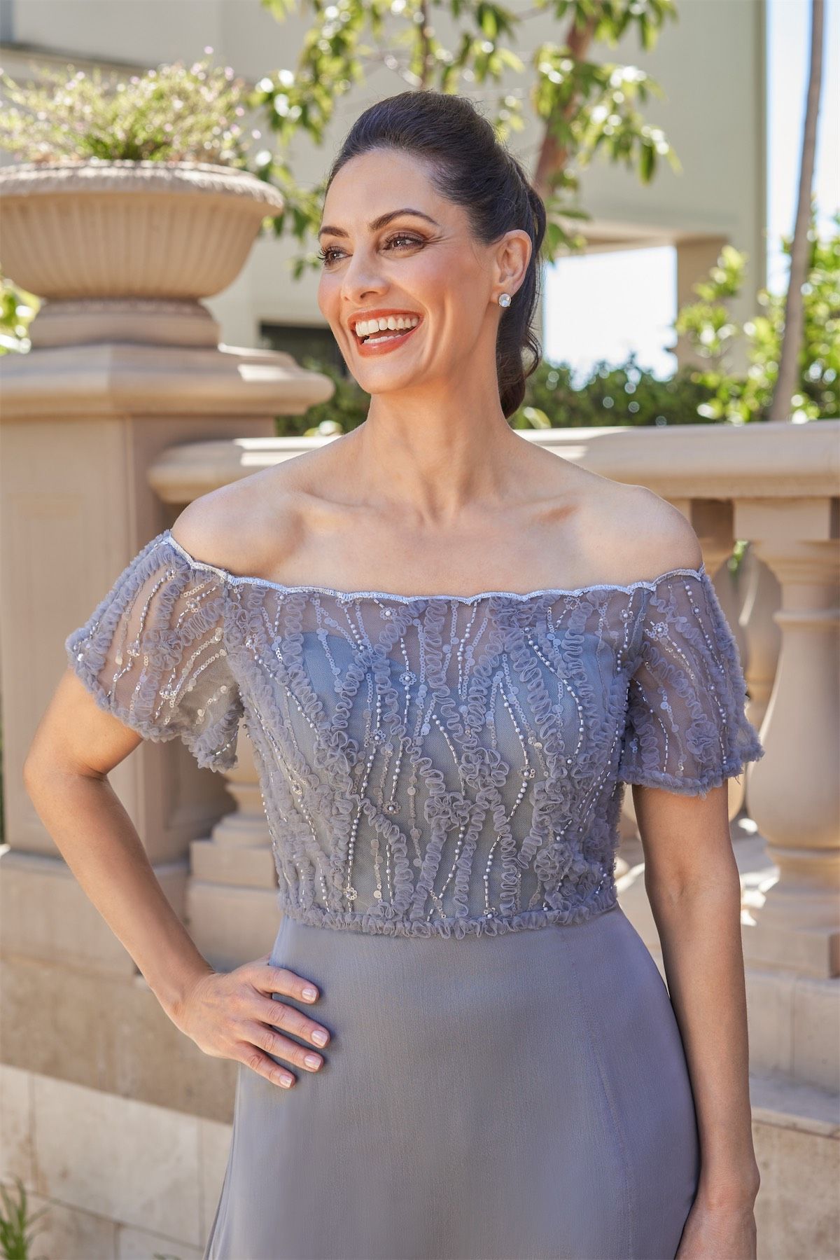 Woman in a white off-shoulder wedding dress smiles in a bridal shop.