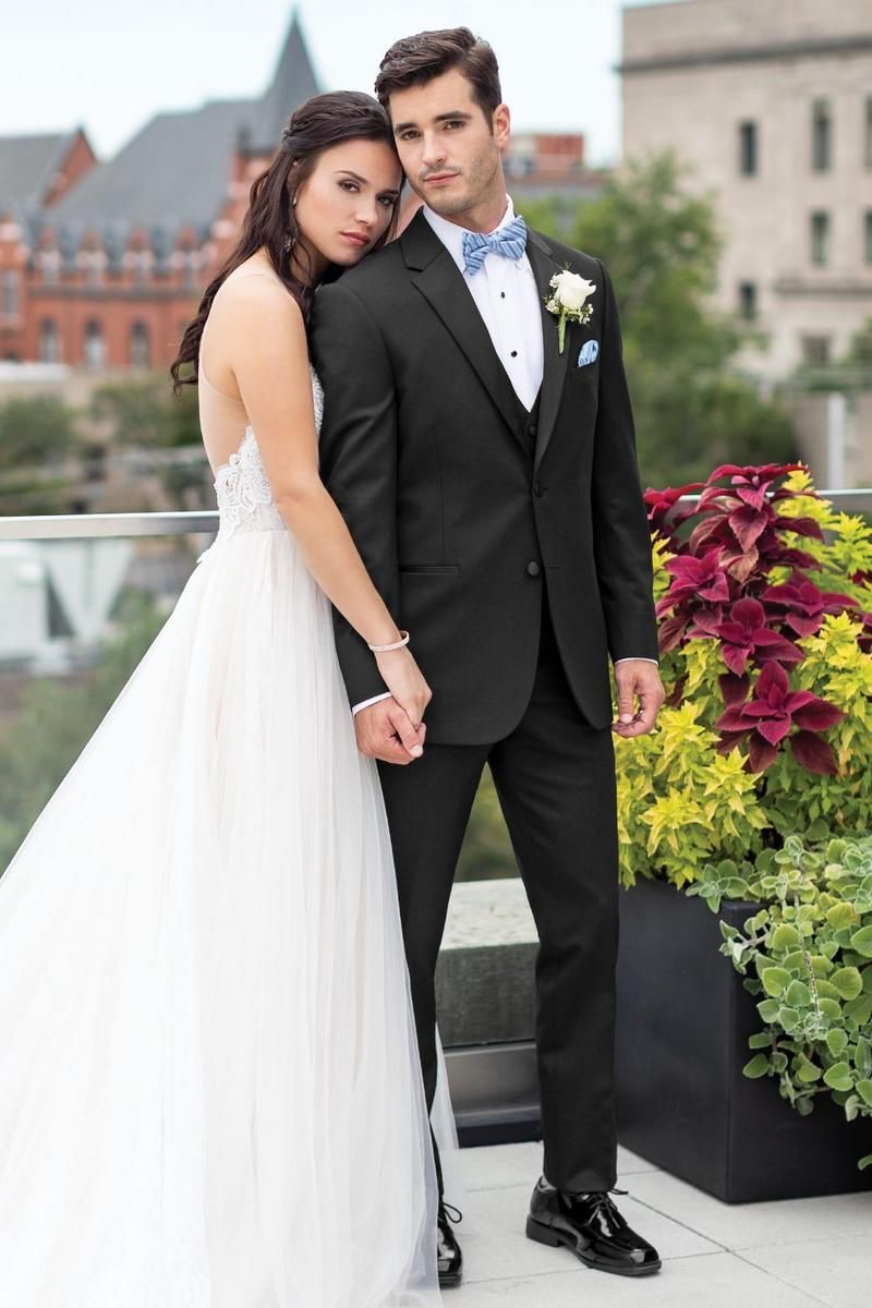 Bride and groom embrace on a rooftop. The groom in black suit and blue bowtie; bride in white gown.