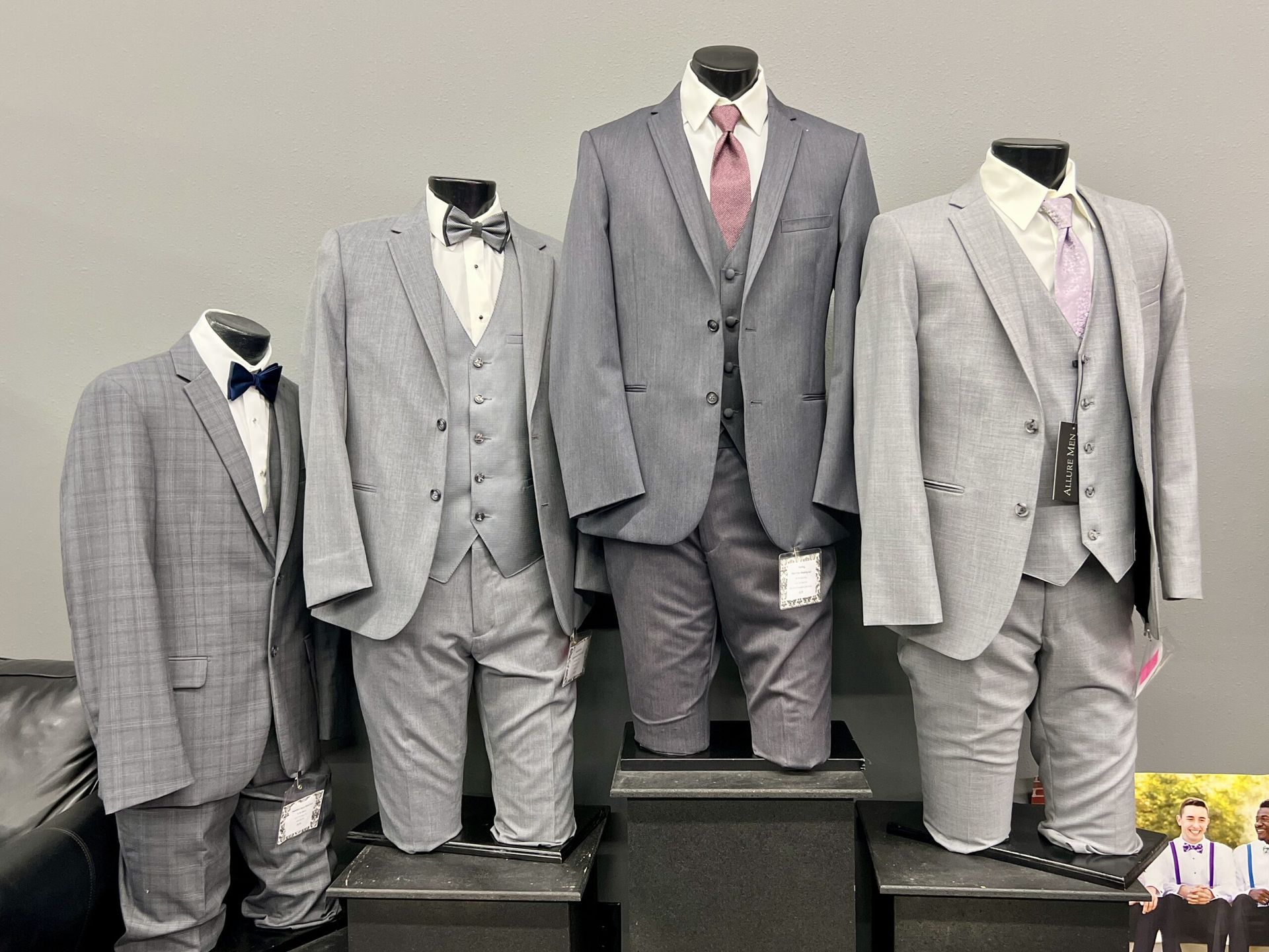 Four gray suits on mannequins. Three have vests and ties. The fourth has a bow tie.