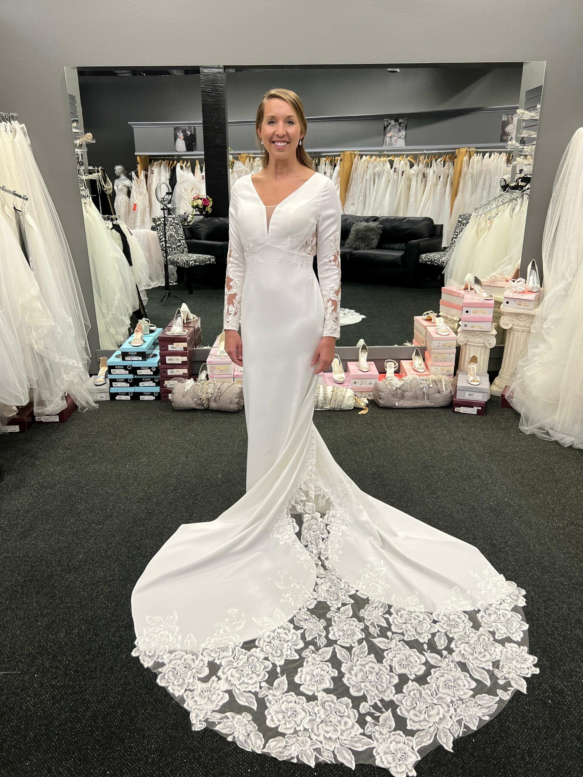 Woman in a white wedding dress with long sleeves and a train, standing in a bridal shop.