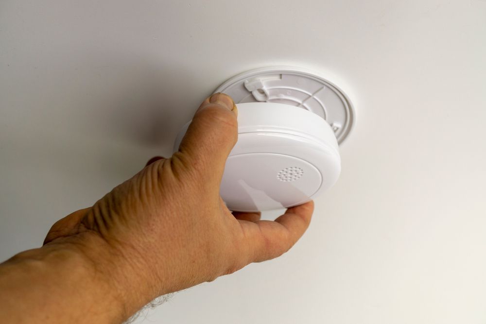 Hand Installing a White Smoke Detector on a Ceiling Mount — Ralph Ottmann Electrical in Sunshine Beach, QLD