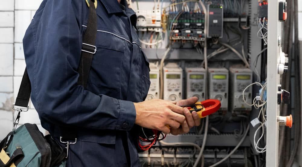 Electrician in Blue Uniform Using a Multimeter on Electrical Panel — Ralph Ottmann Electrical in Pomona, QLD