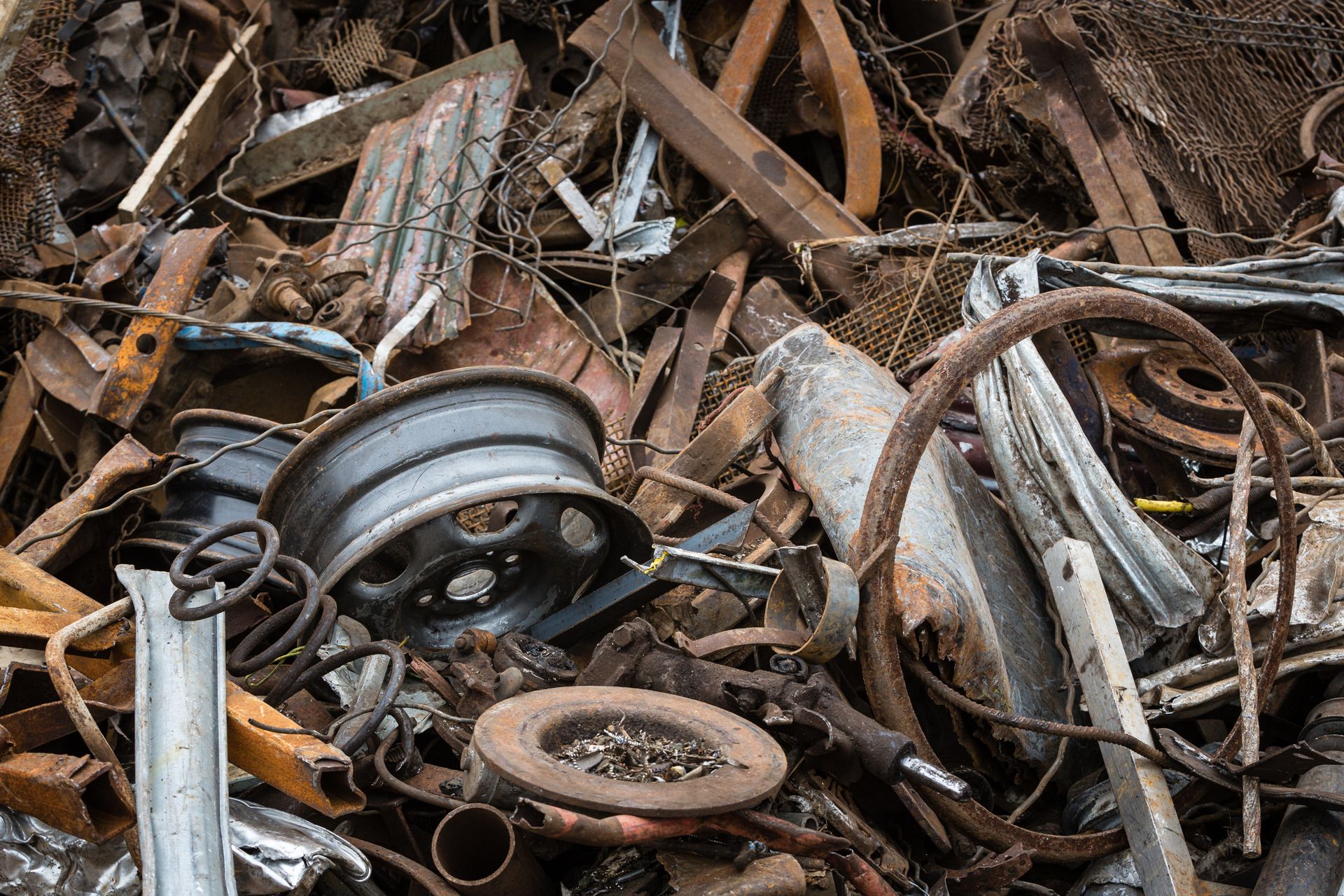 Pile of scrap metal and debris with a rusty wheel rim in a cluttered junkyard.