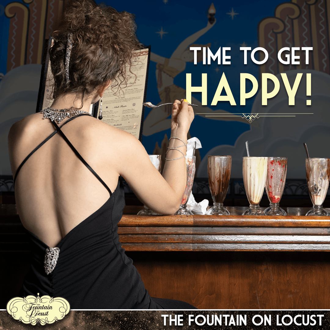 A woman in a black dress sits at a bar with milkshakes and a sign that says time to get happy