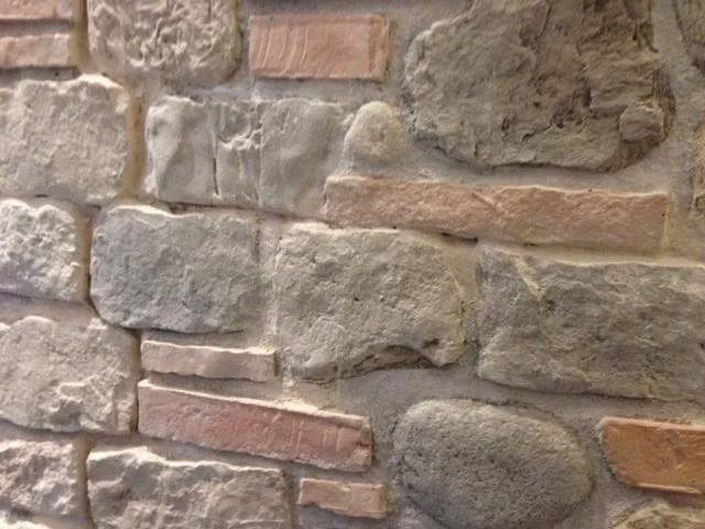 Primo piano di un muro di pietra e mattoni con diverse texture e colori, tra cui grigio, beige e marrone rossastro.