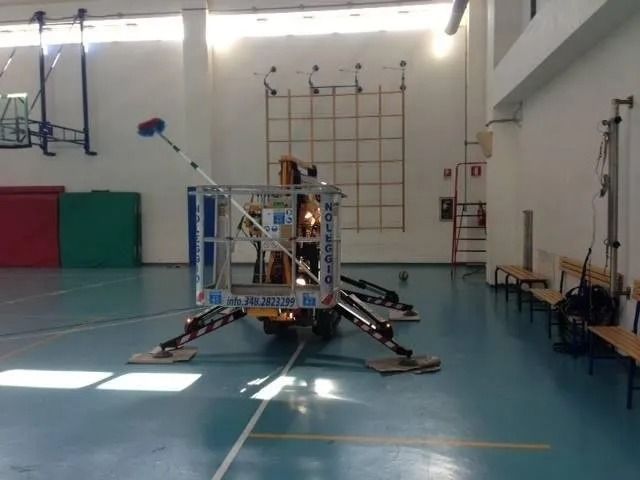 Persona sulla piattaforma elevatrice che pulisce le finestre alte di una palestra.