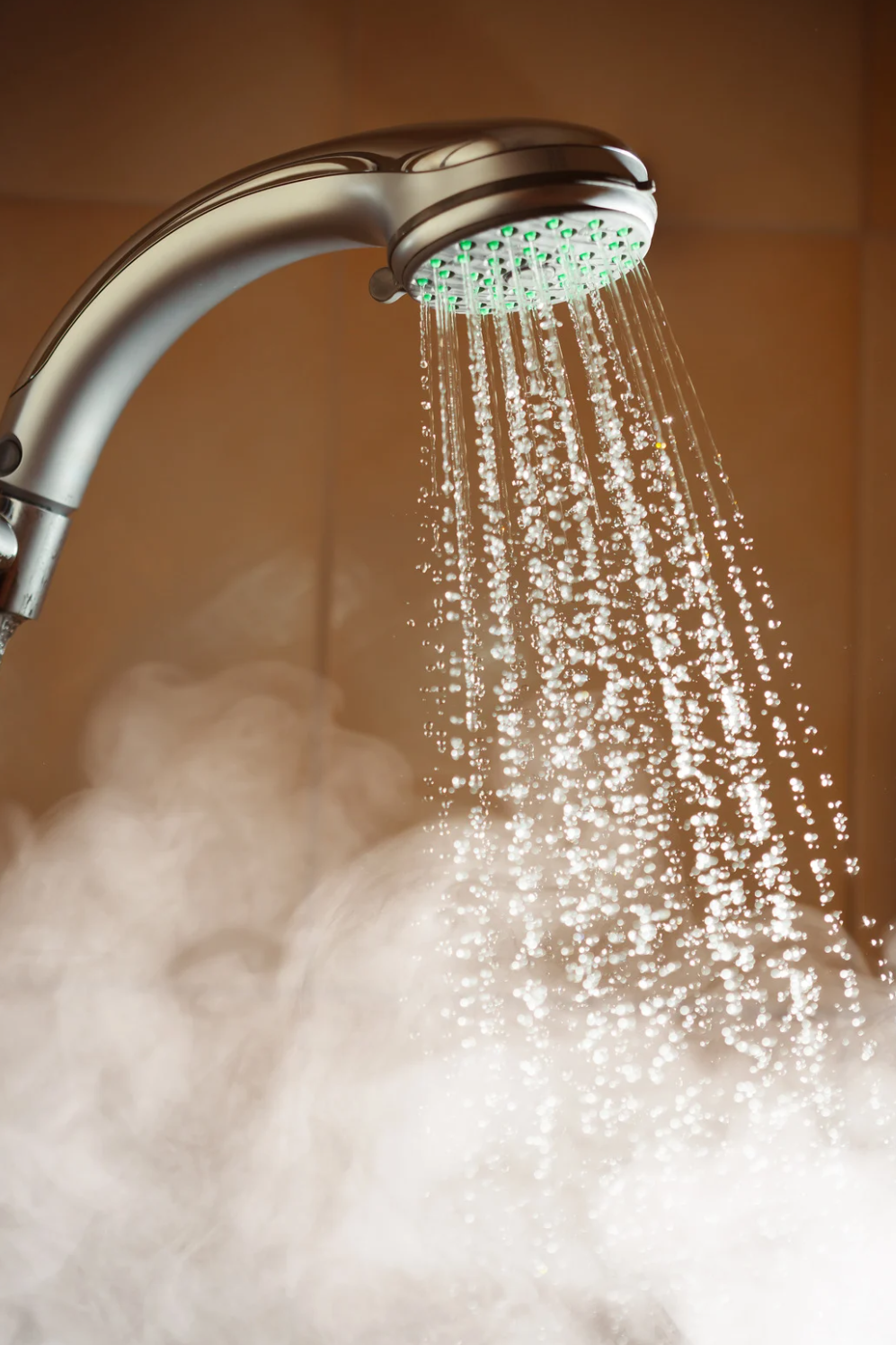 Showerhead with water cascading downwards, creating steam in a tan-colored bathroom.