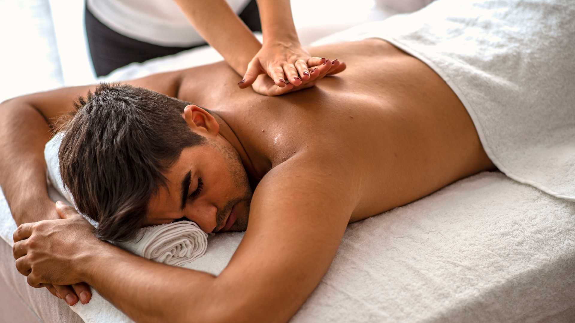 A man is laying on a bed getting a massage from a woman.