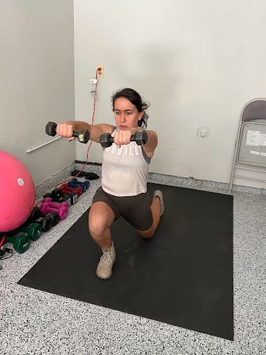 A woman is doing squats with dumbbells in a gym.