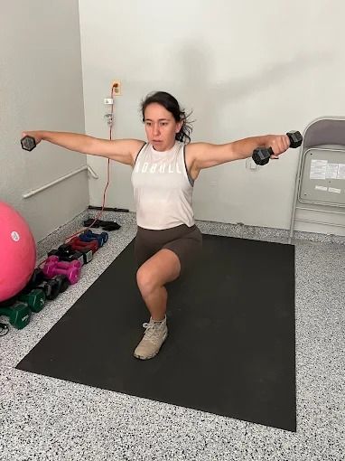 A woman is doing squats with dumbbells in a gym.