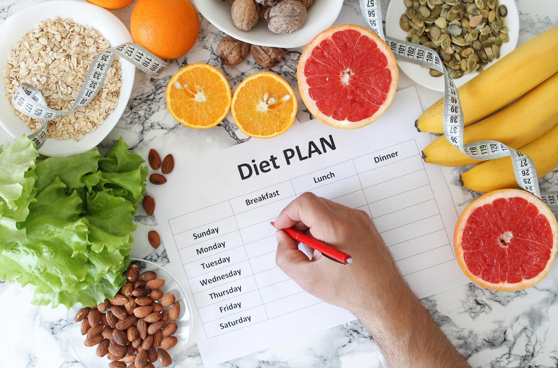 A person is writing on a diet plan surrounded by fruits and vegetables.