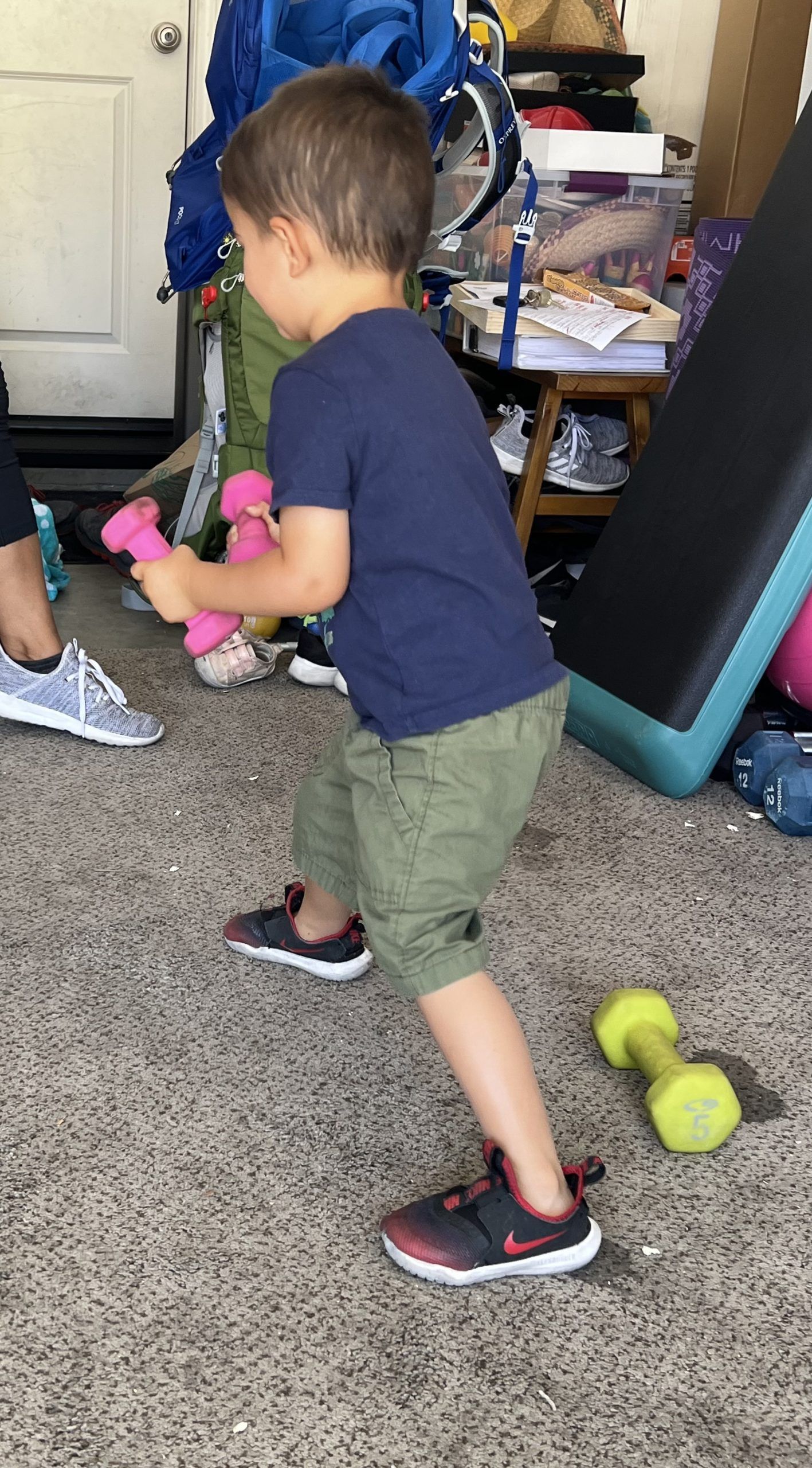A young boy is holding a pink dumbbell in a room.