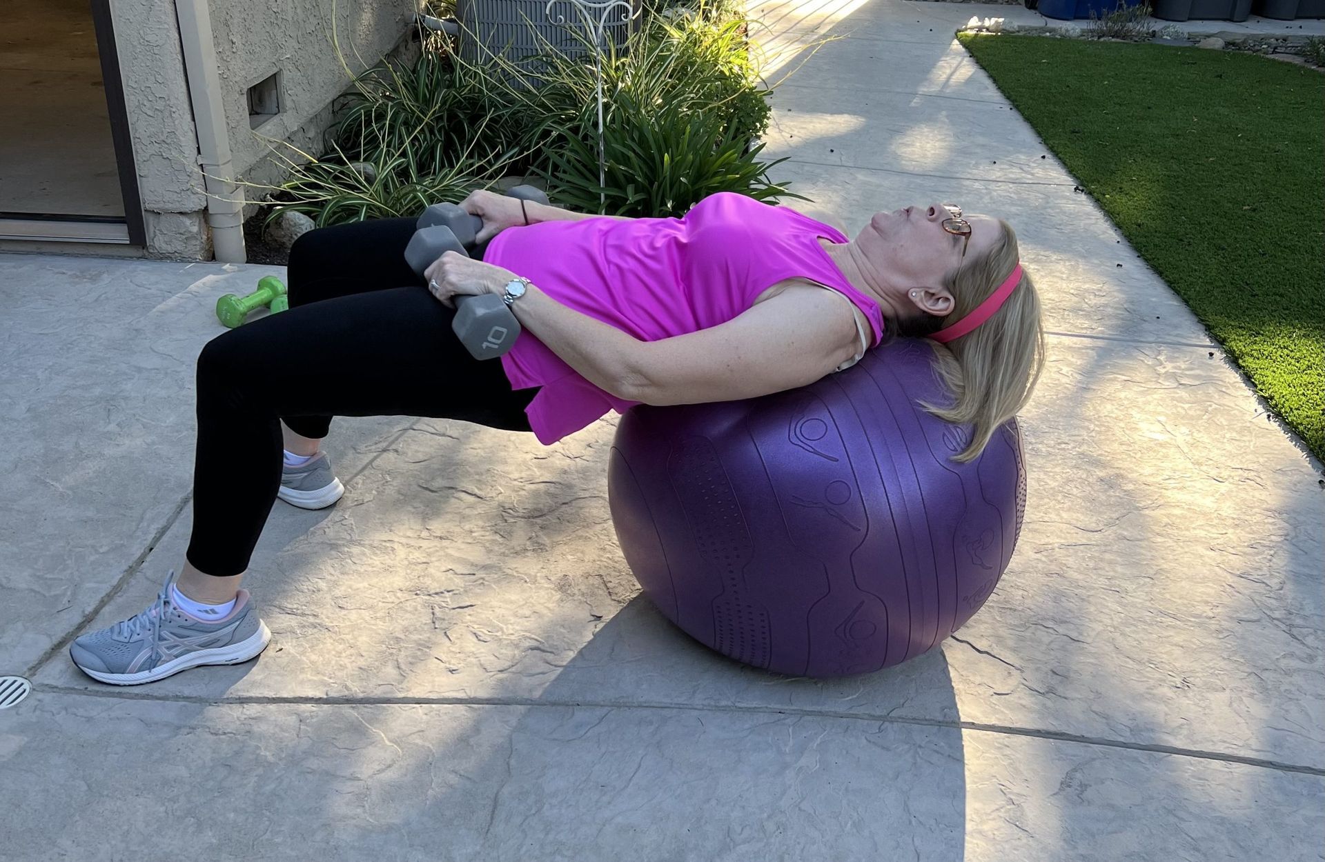 A woman is laying on a purple exercise ball with dumbbells.