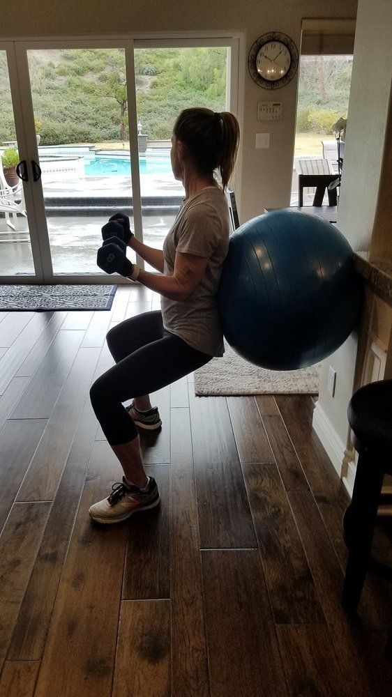 A woman is squatting next to an exercise ball in a living room.