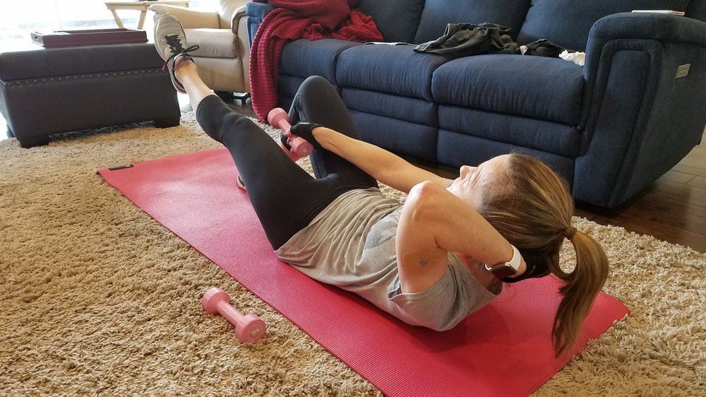 A woman is doing exercises on a yoga mat in a living room.