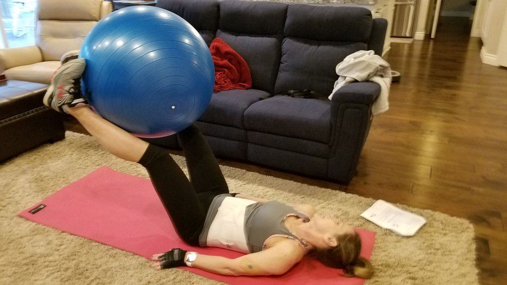 A woman is laying on a yoga mat holding a blue exercise ball.