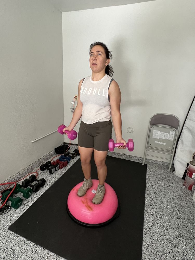 A woman is standing on a pink exercise ball holding dumbbells.