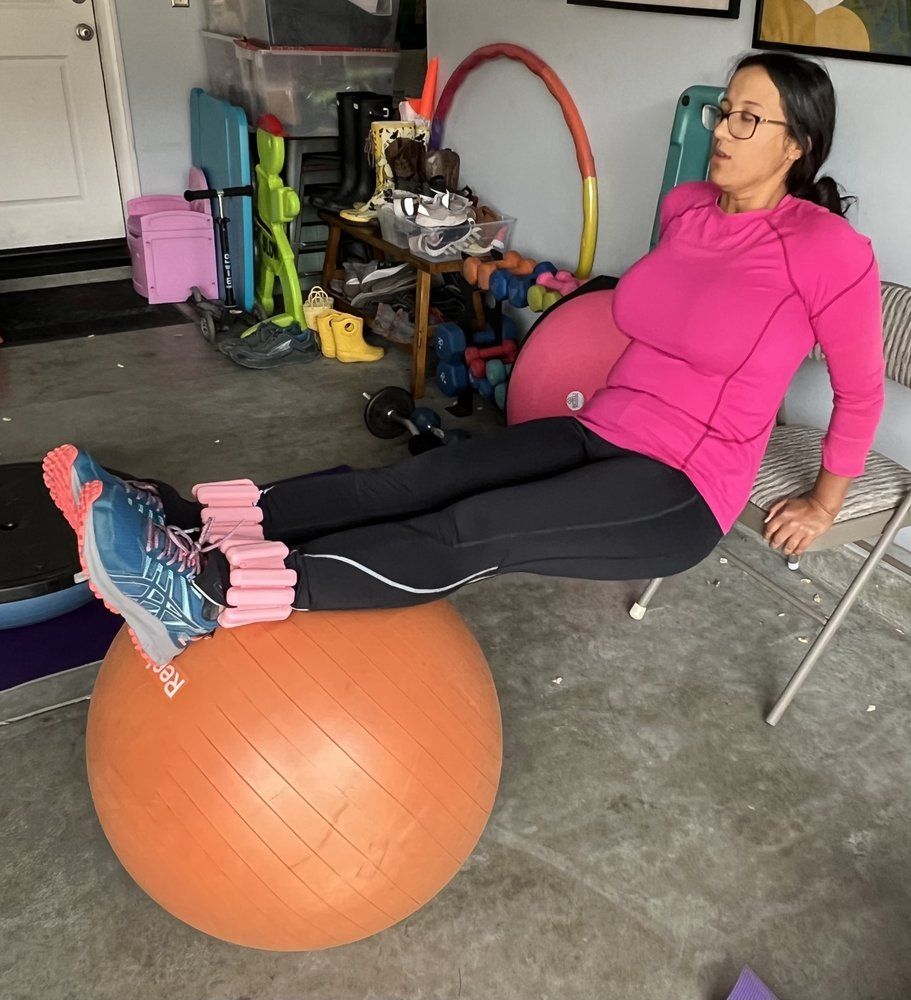 A woman in a pink shirt sits on an orange exercise ball