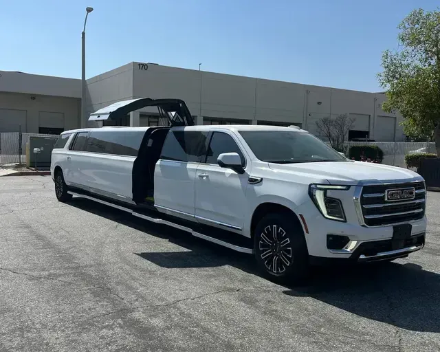 White GMC Yukon limousine parked on asphalt. The door is open on the side.