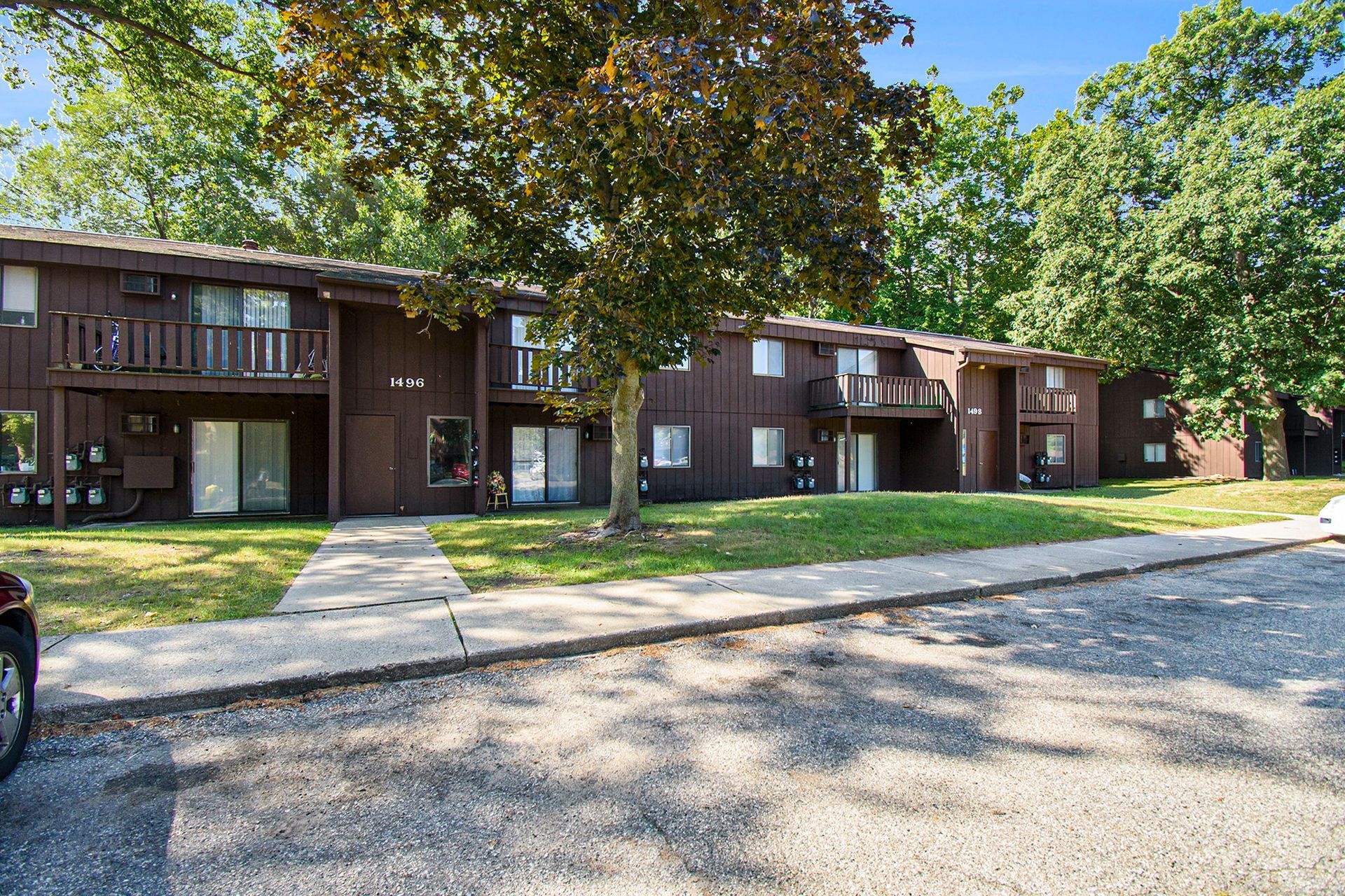 Brown apartment building with balconies, surrounded by trees and green grass.