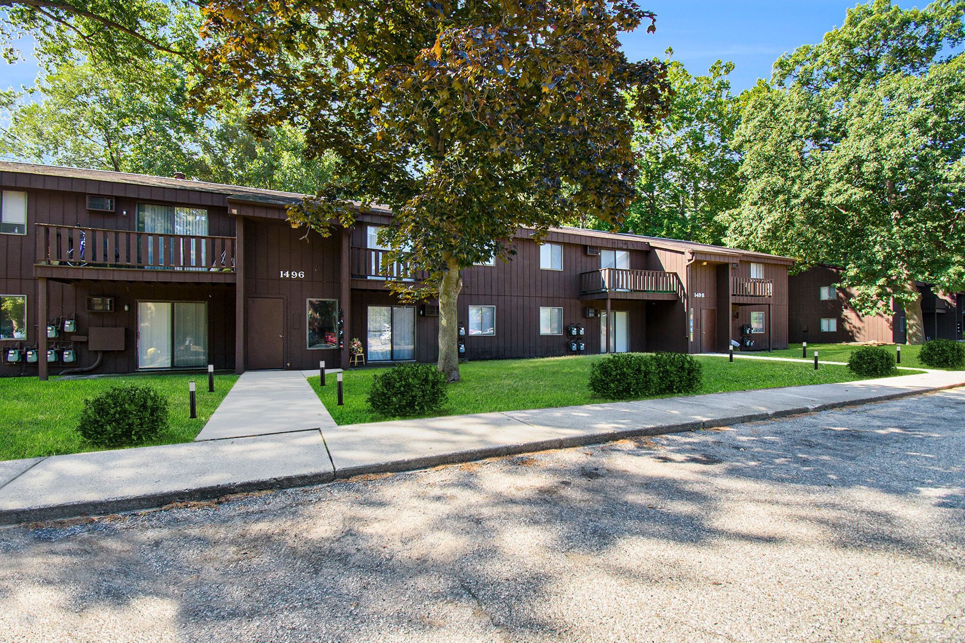 Brown apartment building with green lawn and trees.