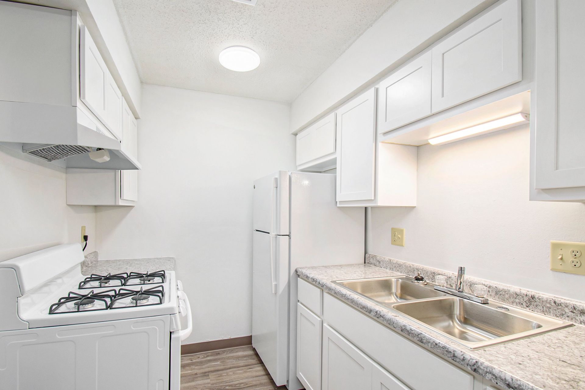 White kitchen with white appliances, cabinets, and a sink with granite countertops.