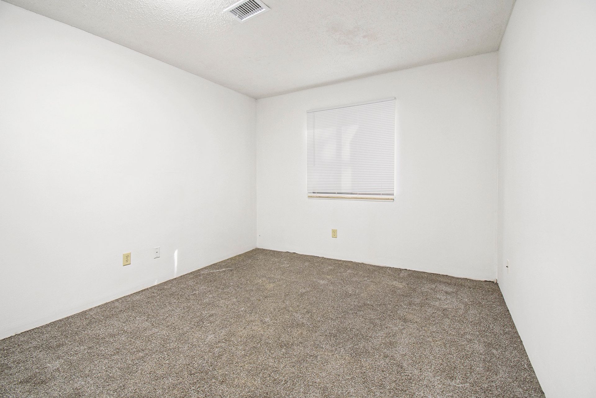 Empty bedroom with beige carpet, white walls, and a window with blinds.