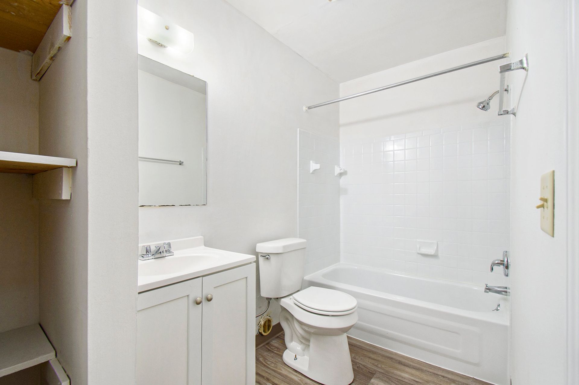 White bathroom with a toilet, vanity, tub, and a small closet.