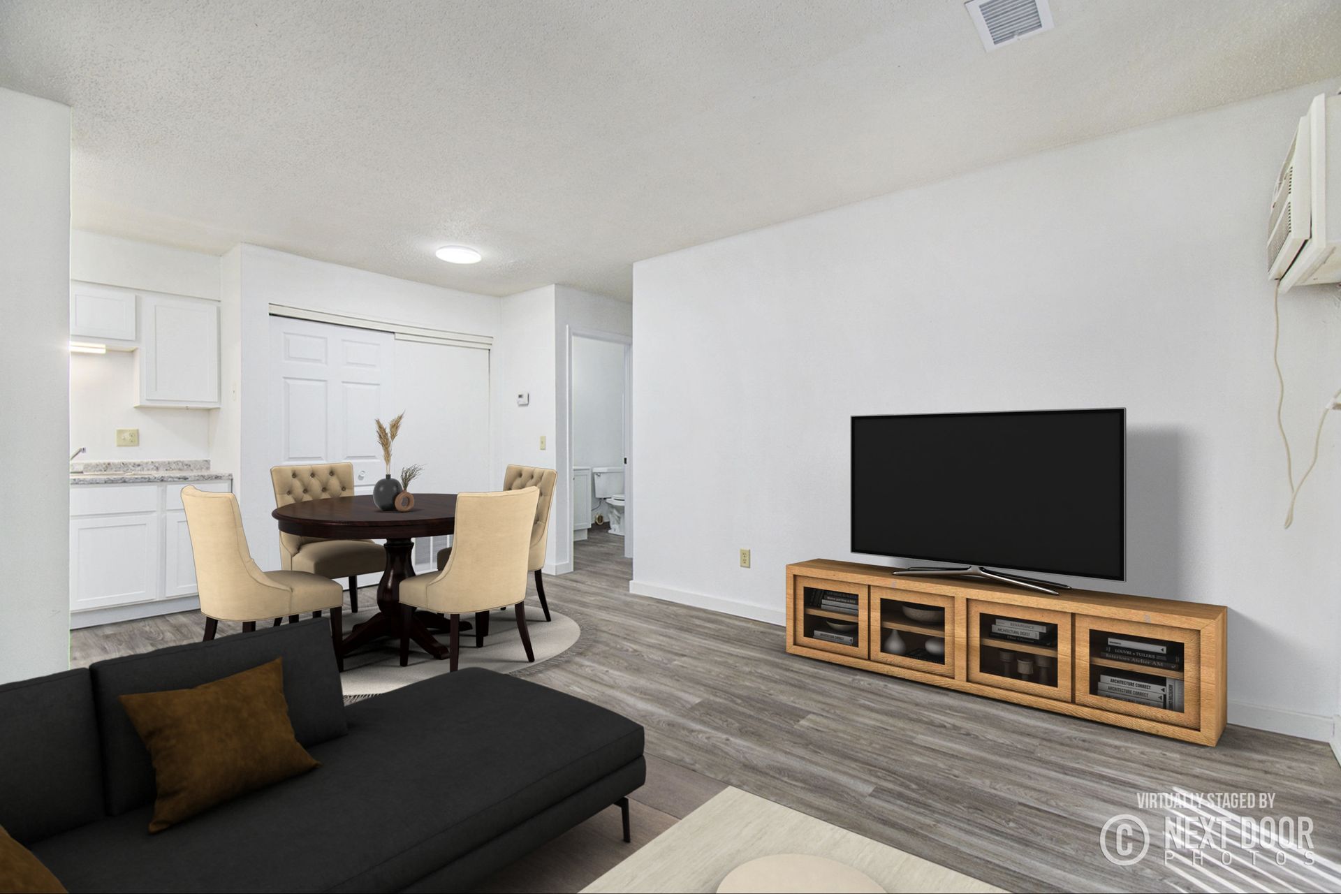 Living room with dining area: black sofa, wooden TV stand, round table, white walls, gray flooring.