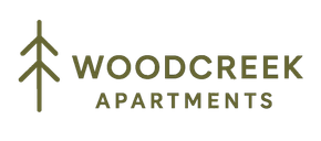 Logo for Woodcreek Apartments: a dark green pine tree next to the words "WOODCREEK APARTMENTS".
