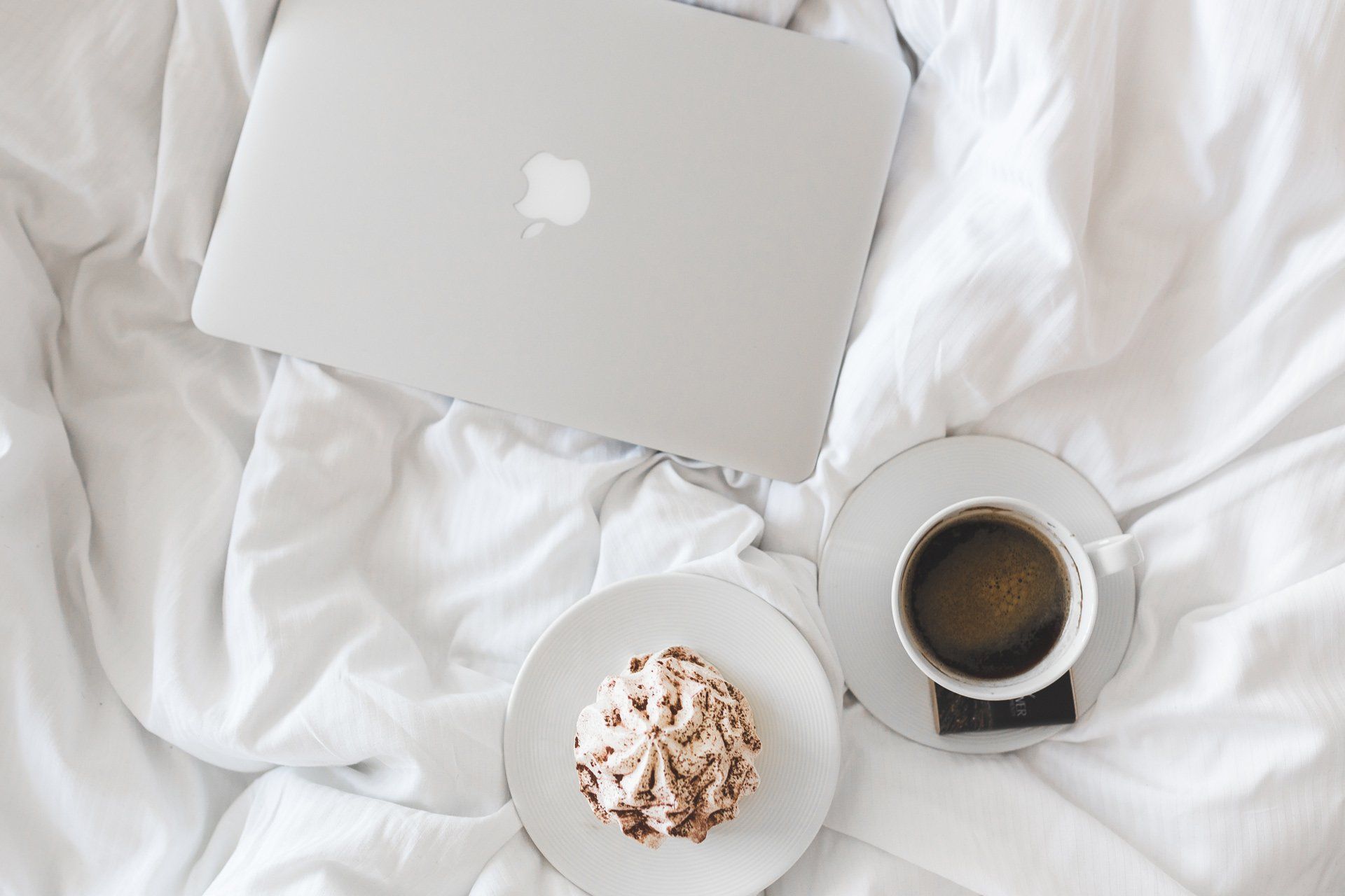 A laptop is sitting on a bed next to a plate of food and a cup of coffee.