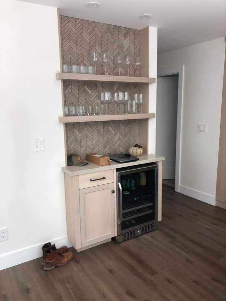 A bar with a wine cooler and glasses on the shelves.