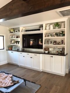 A living room with white cabinets , shelves , and a flat screen tv.