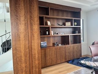 A living room with a large wooden bookshelf and a staircase in the background.