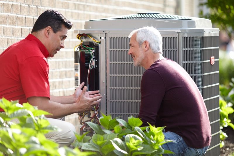 Two men are working on an air conditioner outside of a house.