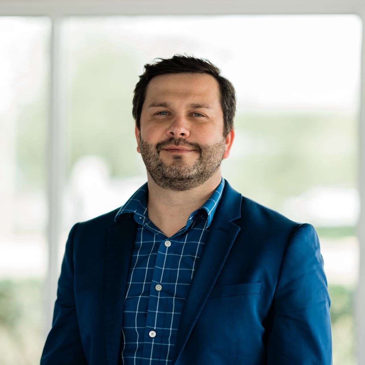A man with a beard wearing a blue jacket and plaid shirt