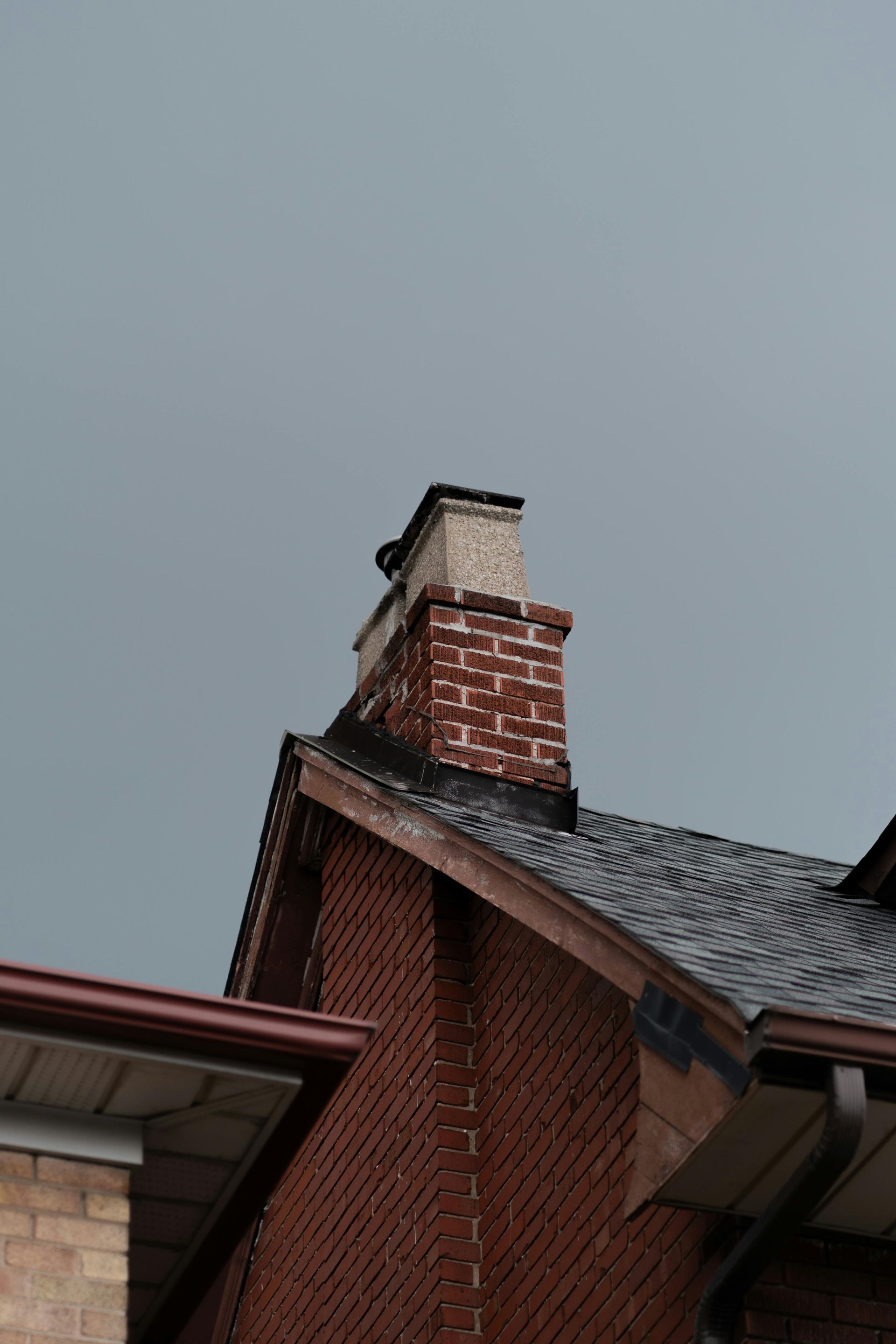 Brick house chimney against a gray sky, with red and white masonry rooflines
