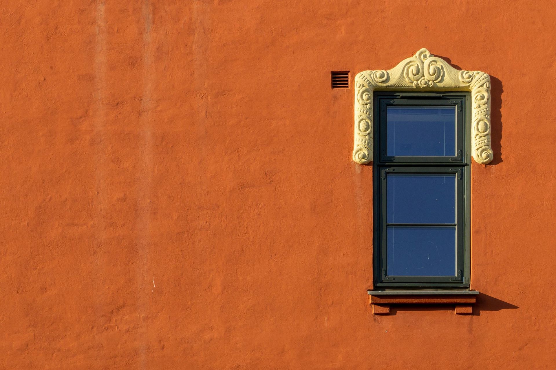 Blue window with ornate cream trim on an orange stucco wall