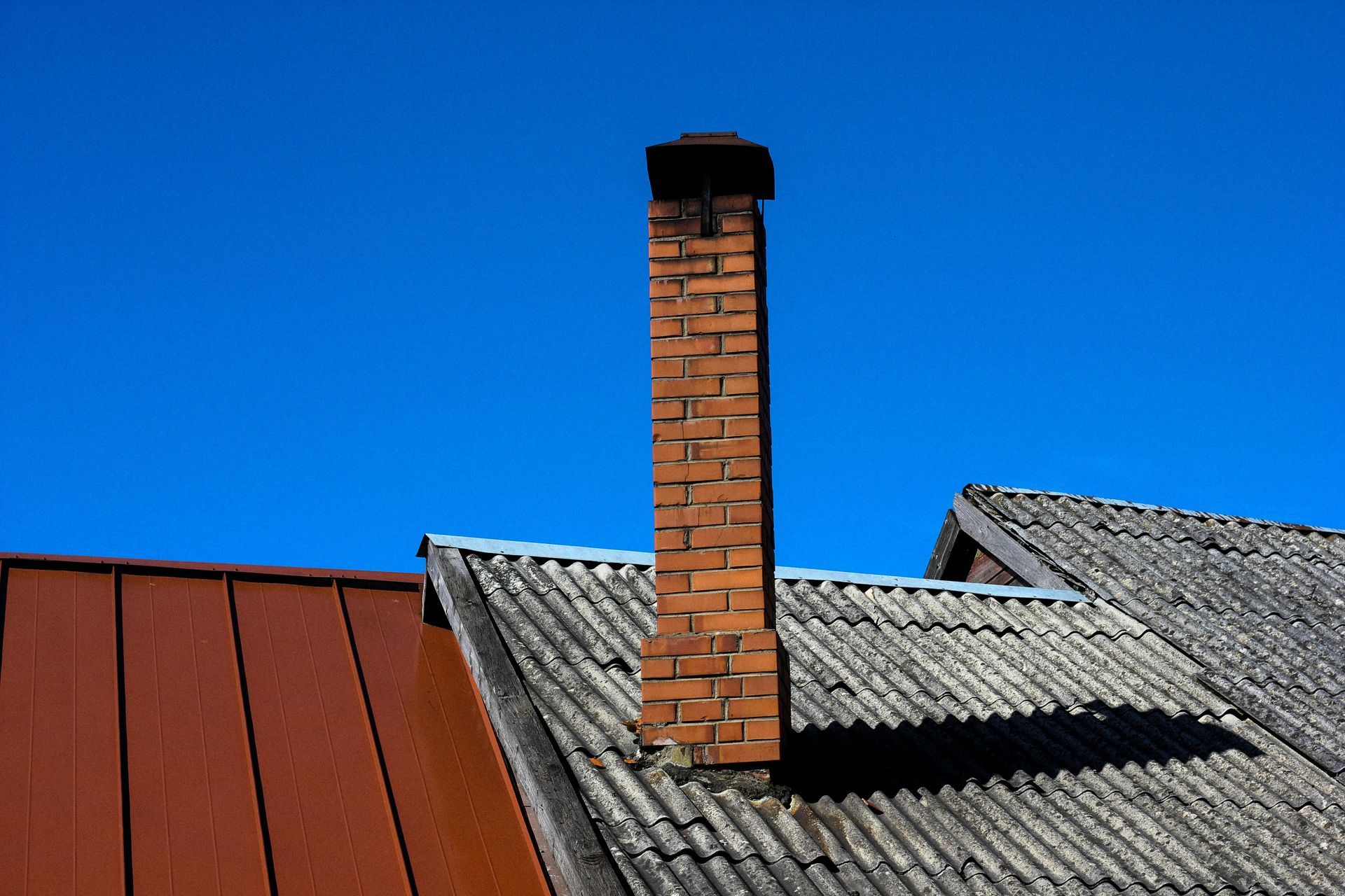 Brick chimney on a gray corrugated roof under a clear blue sky
