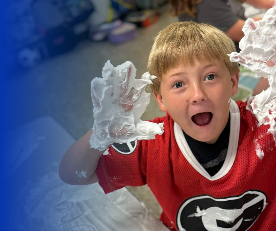 Boy covered in shaving cream, smiling with excitement, red jersey.