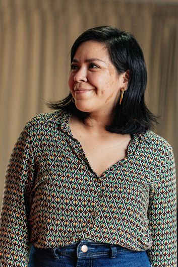 A woman wearing a floral shirt and jeans is smiling.