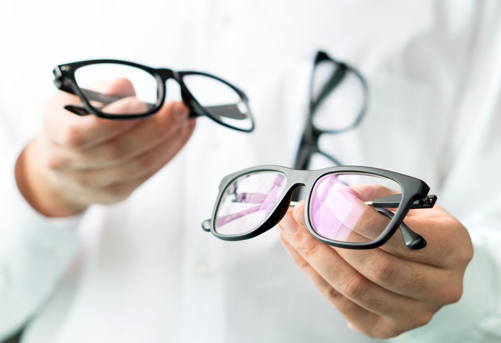 Person Holding Three Pairs of Black Eyeglasses — EyeMax EyeCare in Wallsend, NSW