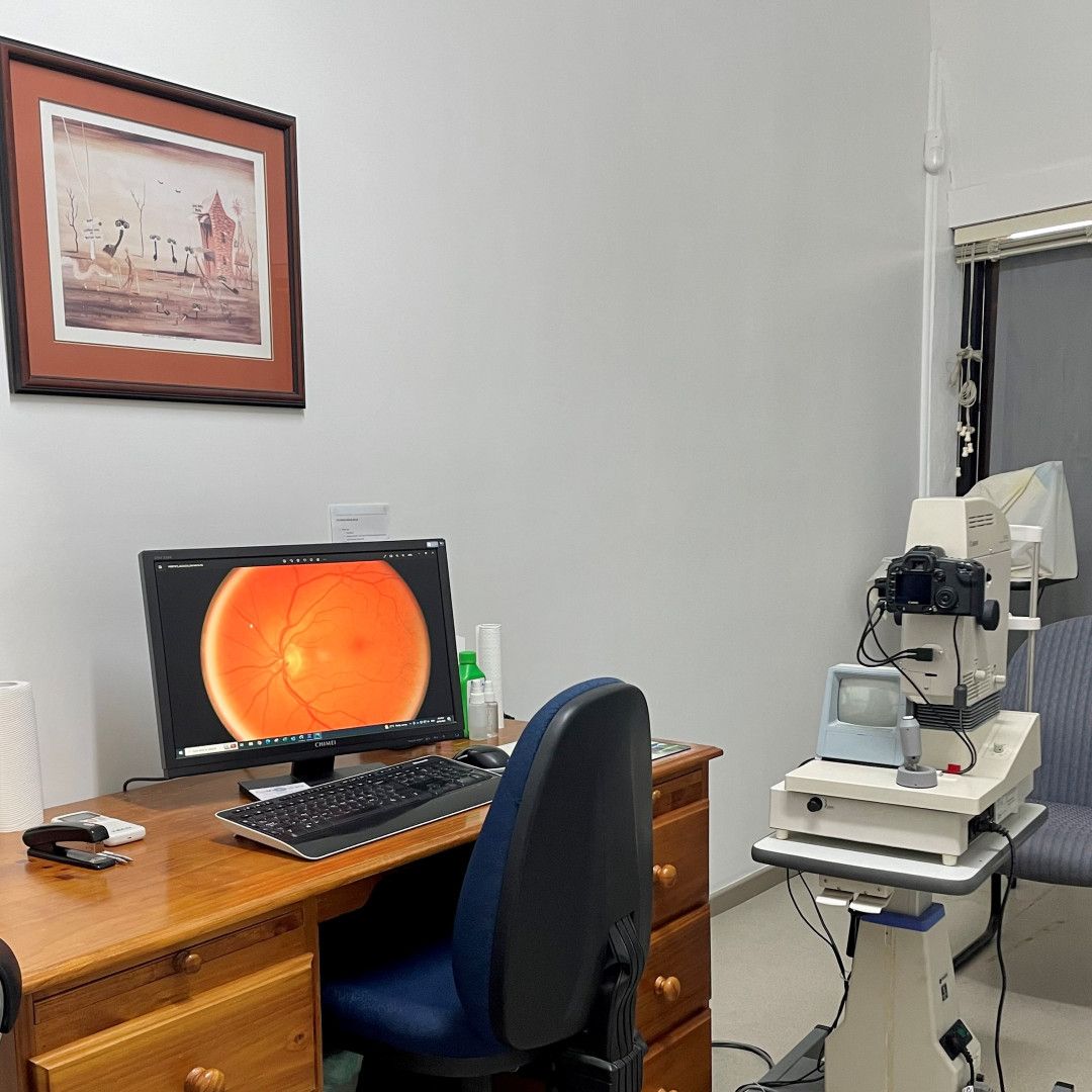 Optometrist's office: desk with computer displaying eye scan, ophthalmic equipment, framed artwork, chair, and white walls. — EyeMax EyeCare in Wallsend, NSW