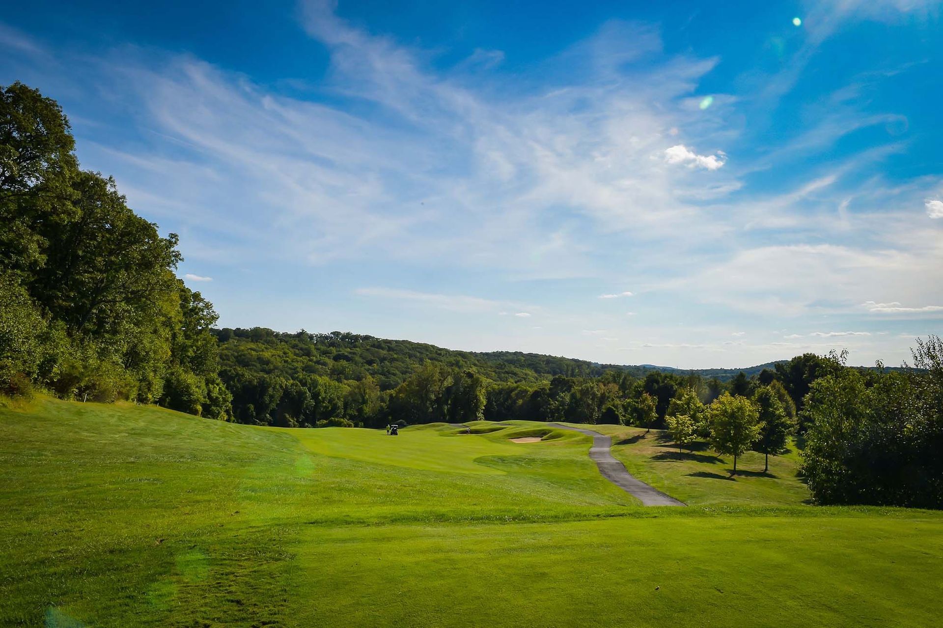 A golf course with trees and a path going through it on a sunny day.