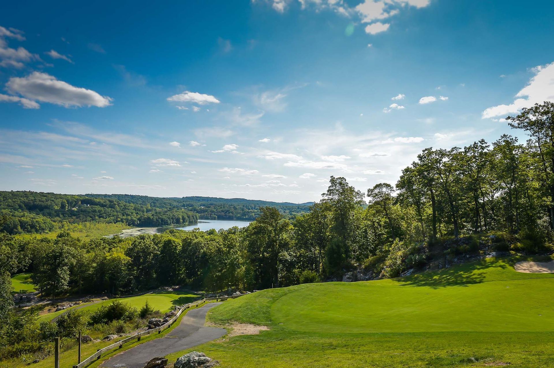 A view of a golf course with trees and a lake in the background.