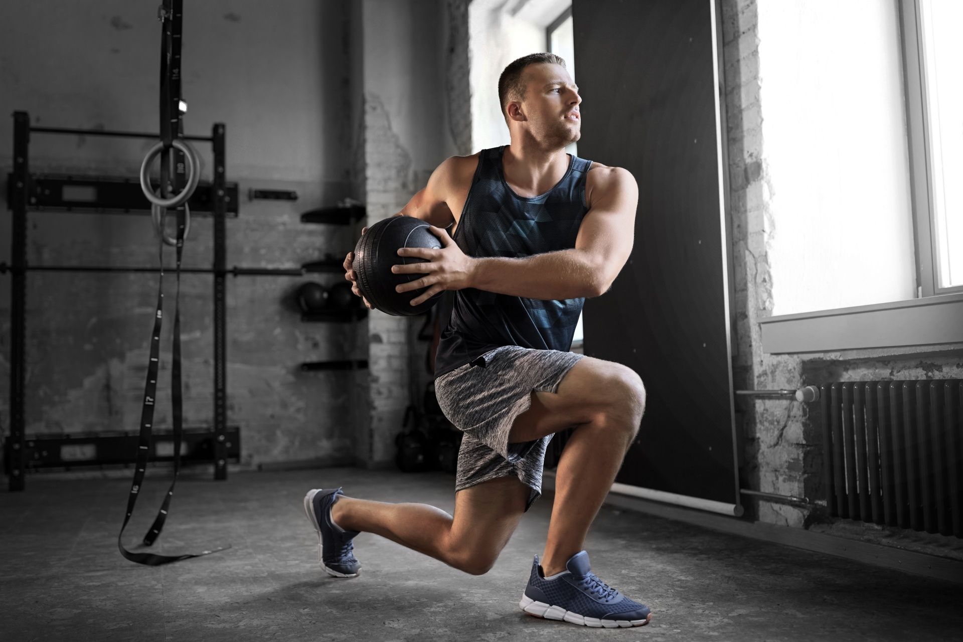 A man is doing lunges with a medicine ball in a gym.